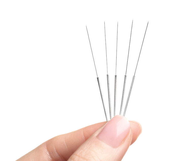 Female fingers with needles for acupuncture on white background